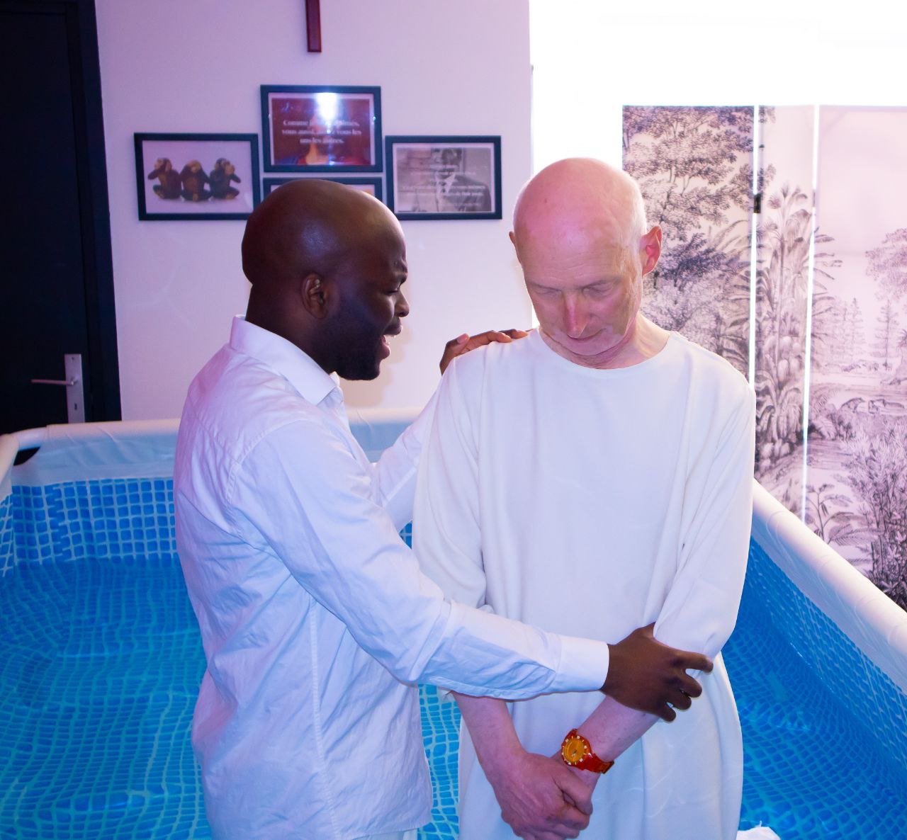 Le pasteur accompagne un frère vêtu de blanc dans le baptistère, avant son baptême