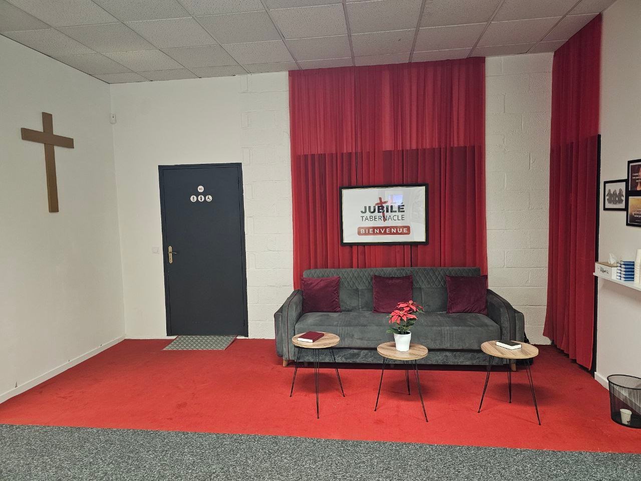 Le salon d'accueil de l'église : canapé, rideaux rouges et écran « Bienvenue »